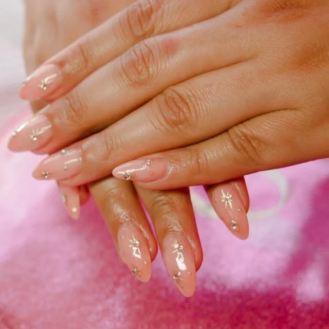 Almond shaped finger nails painted with a nude colour and gold stars with diamonds