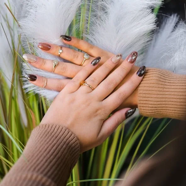 Round shaped finger nails painted with a variety of brown colours and glitter on top