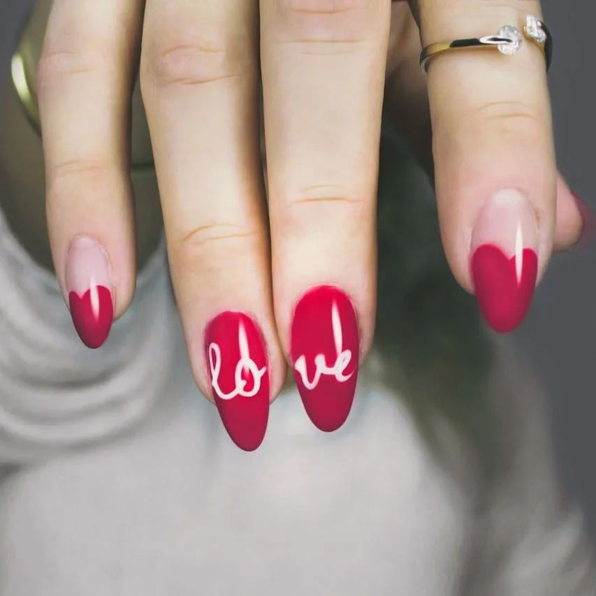 Almond shaped finger nails, painted red with the word, love, written across two nails