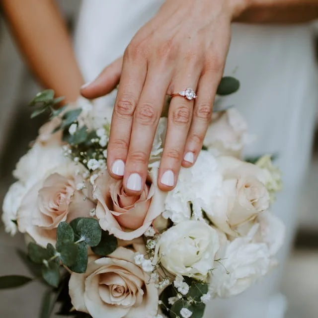 Short painted light pink nails in front of a bouquet of flowers